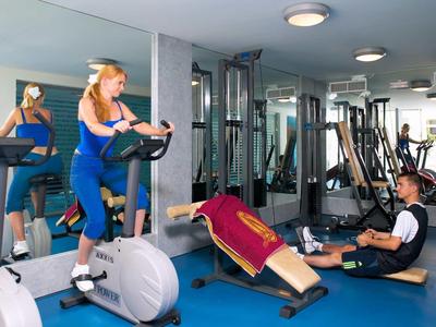 Moderne Fitnessraum mit verschiedenen Trainingsgeräten und Menschen beim Workout.