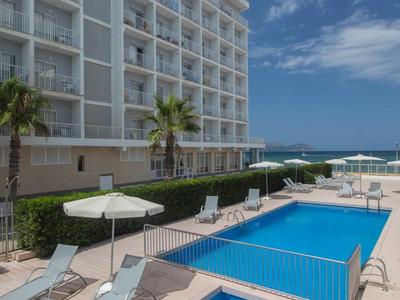 Moderner Hotelpool mit Liegestühlen, Sonnenschirmen und Meerblick unter blauem Himmel.