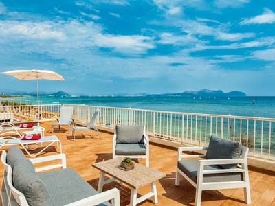 Terrasse mit modernen Sesseln und Liegestühlen mit Blick auf das Meer bei klarem Himmel.