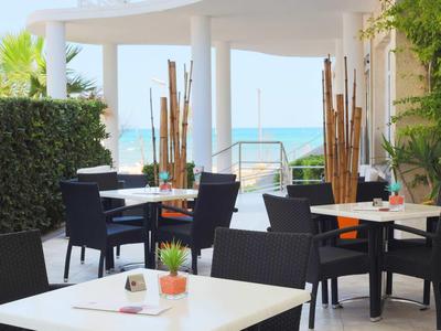 Outdoor-Restaurantbereich mit schwarzen Stühlen und Tischen mit Blick auf das Meer.