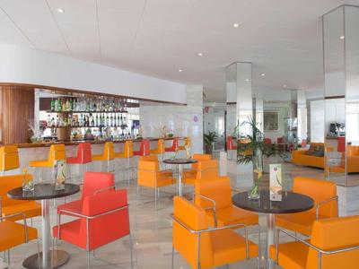 Moderner Hotelbarbereich mit orangefarbenen und roten Stühlen und runden Tischen.