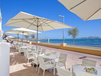 Terrasse mit weißen Stühlen und Sonnenschirmen am Meer an einem sonnigen Tag.