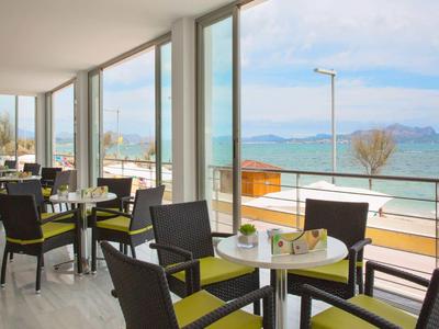 Helles Café mit Glasfront und Blick auf See und Berge im Hintergrund.