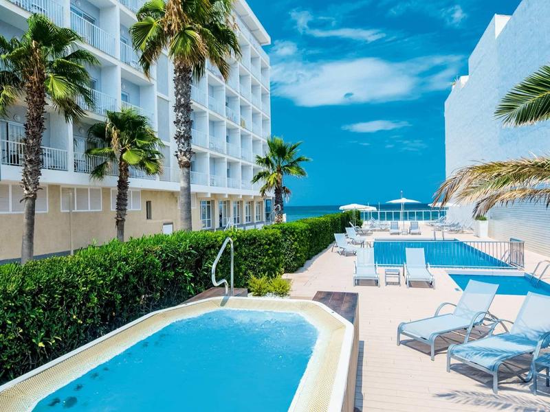 Terrasse d'hôtel avec piscine, chaises longues et vue sur la mer par jour ensoleillé