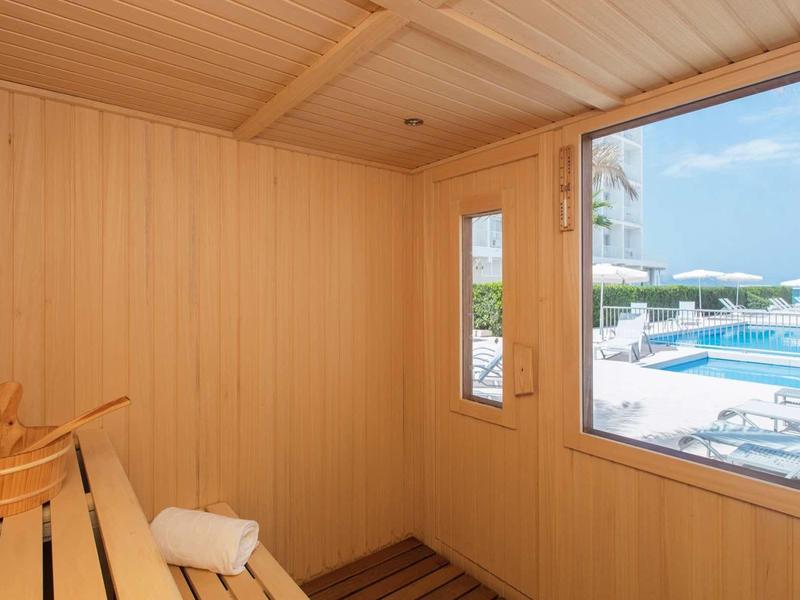 Sauna en bois avec fenêtre donnant sur une piscine et des transats.