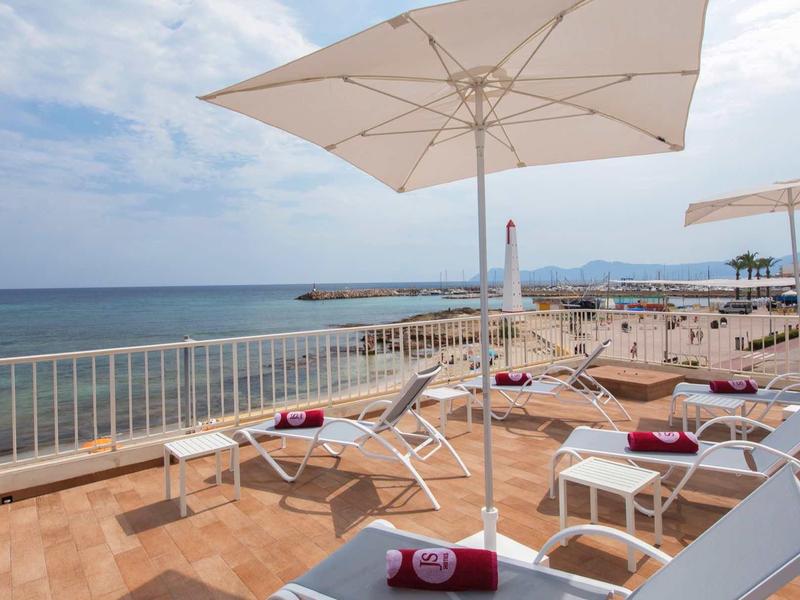 Terrasse avec chaises longues et parasols offrant une vue sur la mer par une journée ensoleillée.