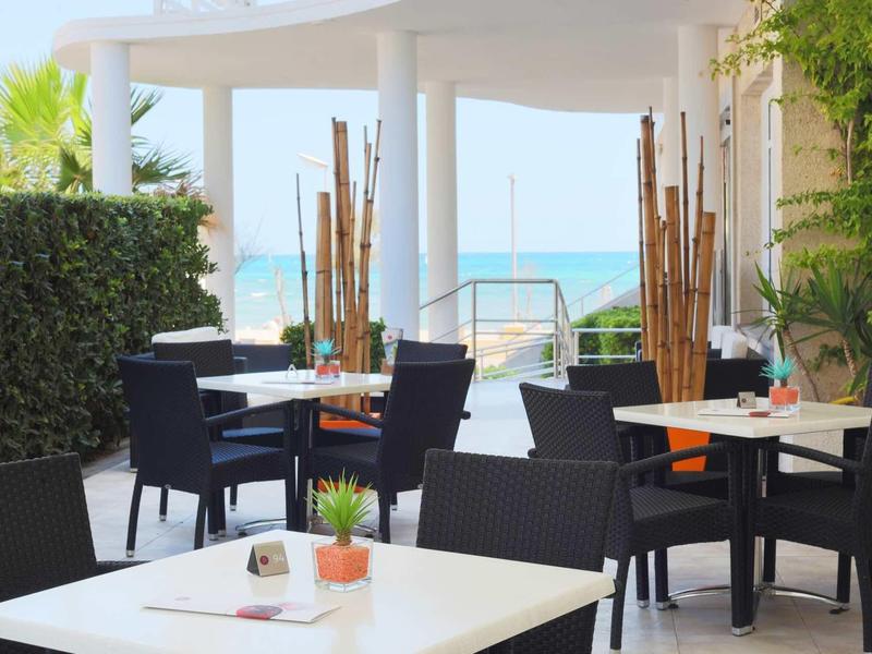 Terrasse d'hôtel avec tables, chaises et vue sur la mer par temps ensoleillé.