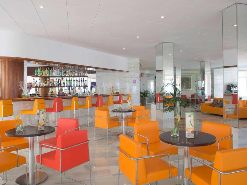 Bar d'hôtel moderne avec fauteuils orange et tables noires, ambiance lumineuse.