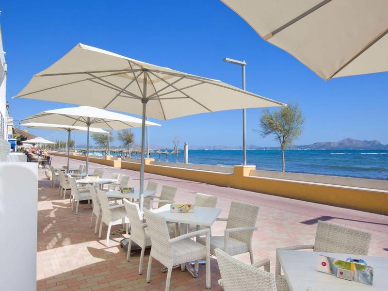 Terrasse extérieure avec chaises blanches et parasols au bord de la mer par une journée ensoleillée.
