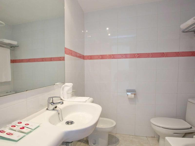 Salle de bain d'hôtel lumineuse avec lavabo, toilettes et grands miroirs.