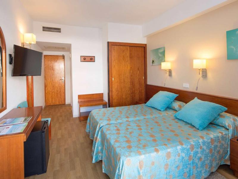 Chambre d'hôtel lumineuse avec deux lits simples, meubles en bois et télévision murale.