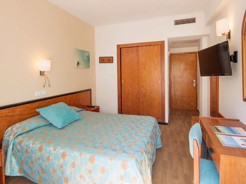 Chambre d'hôtel lumineuse avec lit double, meubles en bois et télévision murale.