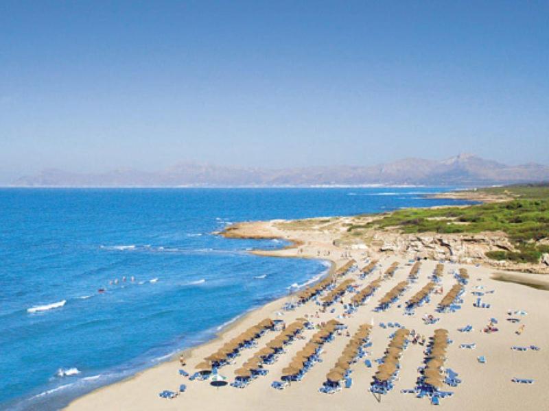 Weitläufiger Sandstrand mit Sonnenschirmen und blauem Meer unter klarem Himmel.