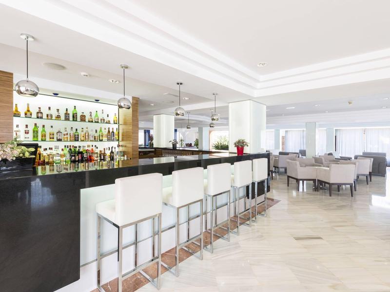 Elegante Hotelbar mit weißen Barhockern und einem gut bestückten Regal im Hintergrund.