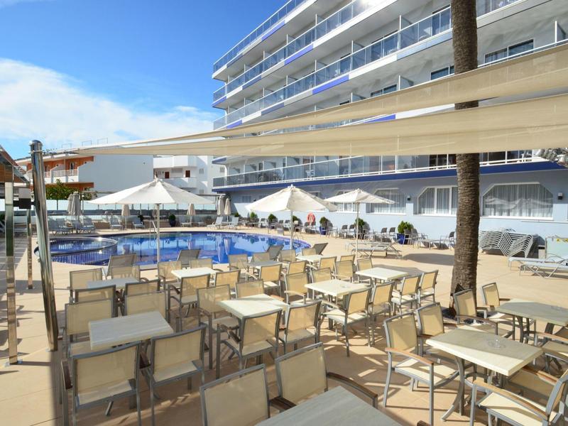 Hotelpoolbereich mit vielen Stühlen und Tischen, Sonnensegeln und modernen Gebäuden im Hintergrund