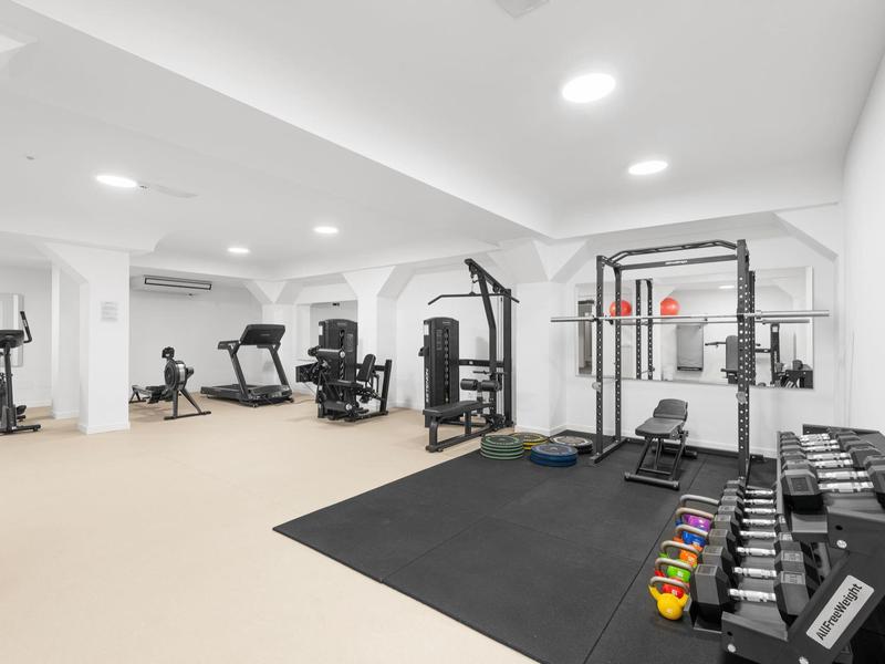 Moderner Fitnessraum mit Hanteln, Kardiogeräten und Kraftmaschinen in hellem Raum.