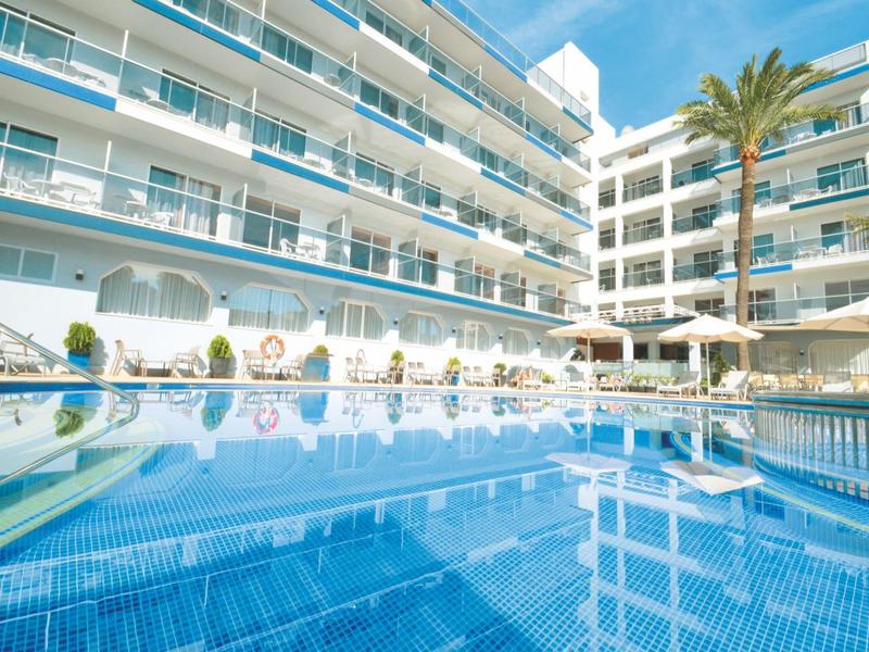 Hotel mit großem Außenpool, Sonnenschirmen und Palmen bei klarem Himmel