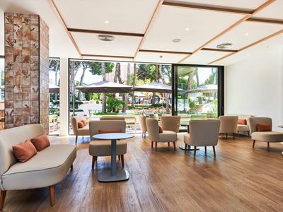 Bright, modern hotel lobby with wooden flooring, seating areas, and large windows.
