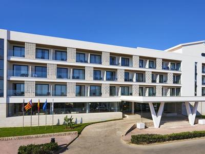 Modern three-story hotel building with large glass facade and white exterior under clear sky.