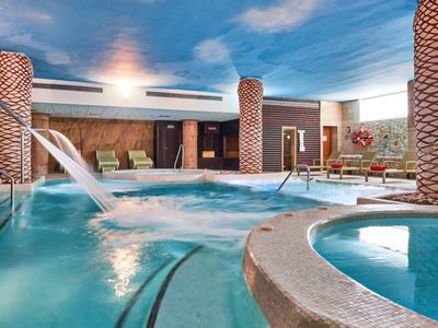 Indoor hotel area with pool, hot tubs, and water features under a blue sky.