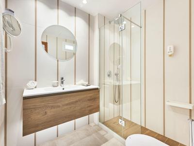 Modern bathroom with wooden vanity, round mirror, and glass shower.