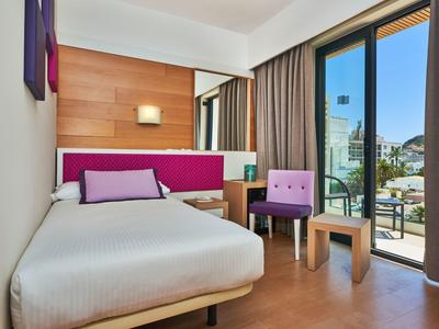 Modern hotel room with single bed, chair, table, and balcony view.