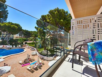 Balcony with chairs and artwork overlooking pool and garden in a hotel.