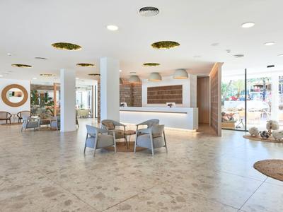 Heller, moderner Hotel-Lobbybereich mit Sitzgelegenheiten, Rezeption und großen Fenstern.