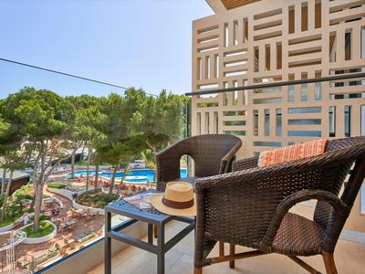 Balcony with rattan chairs and small table overlooking a pool and pine trees.