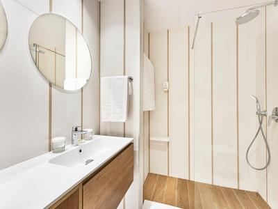 Modern bathroom with double sink, two round mirrors, and walk-in shower with wooden floor.