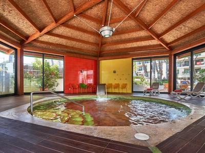 Interior of a hotel with a round hot tub, large windows, and wooden flooring.