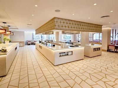 Jasna, nowoczesna restauracja bufetowa z centralną wyspą i nakrytymi stołami w tle.