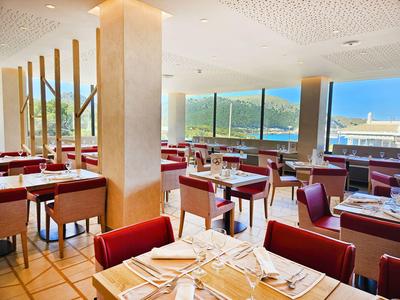Jasna sala restauracyjna w hotelu z czerwonymi tapicerowanymi krzesłami i dużymi oknami z widokiem na góry.