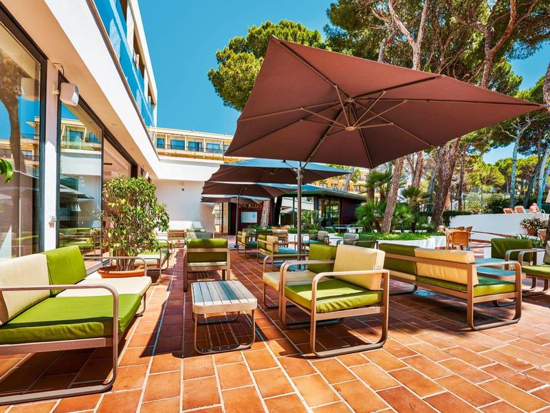Outdoor lounge area with green cushions, sun umbrellas, and terracotta flooring.