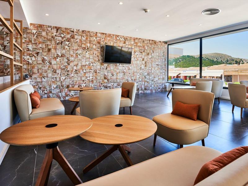 Elegant hotel lounge area with stone wall, cozy chairs, and views of pool and mountains.