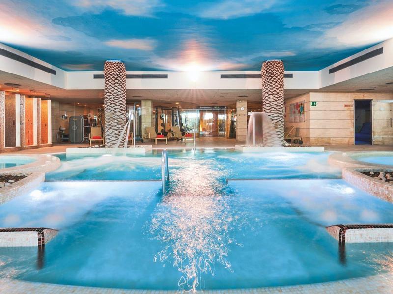 Modern indoor swimming pool with jacuzzi and blue illuminated water in a luxurious setting.
