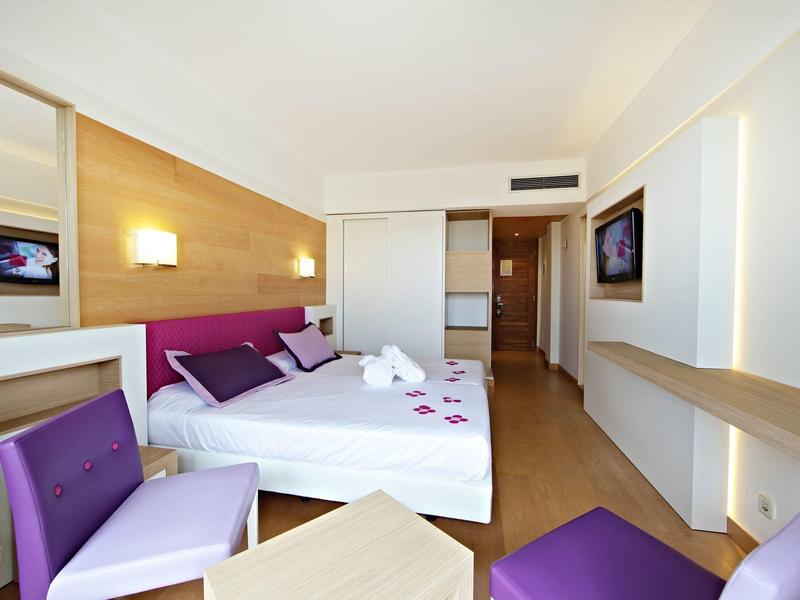Modern hotel room with double bed, purple accents, and wooden flooring.