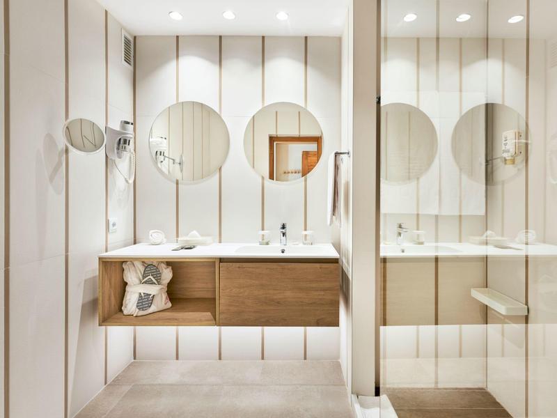 Modern bathroom area with white tiles, wooden cabinet, and three round mirrors.