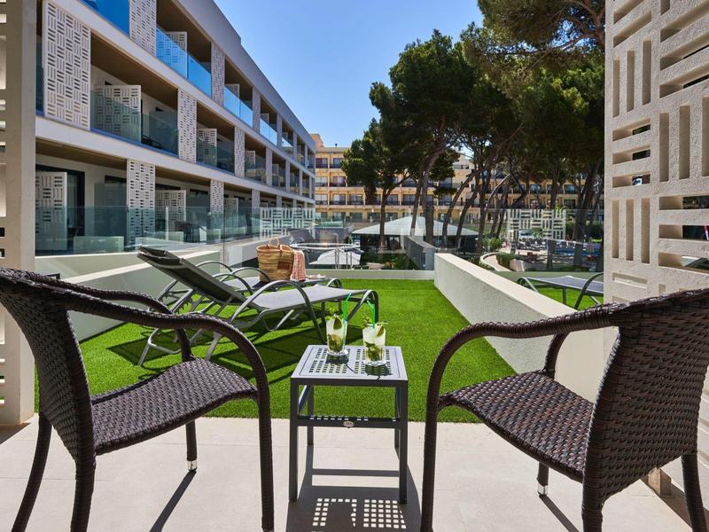 Terrace with chairs, table and view of hotel pool and garden under clear sky.