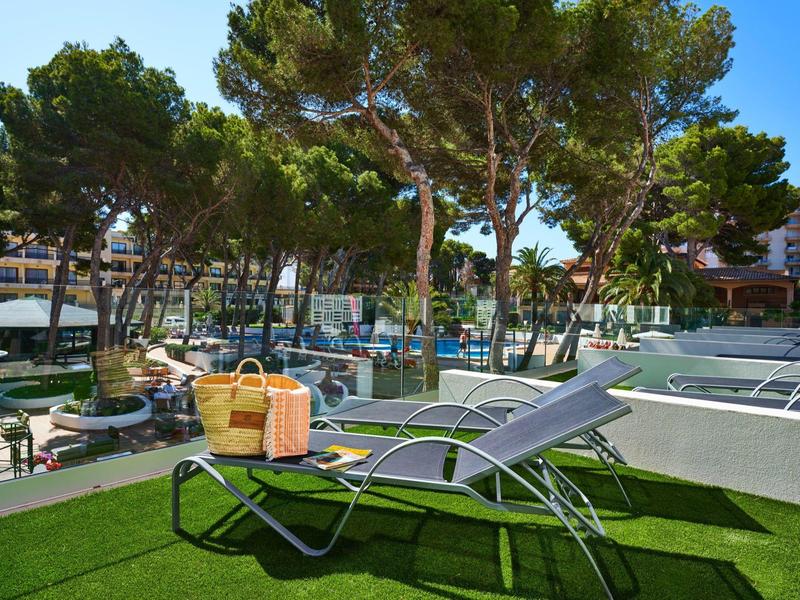 Two lounge chairs with towels and basket on green grass near a pool and trees.