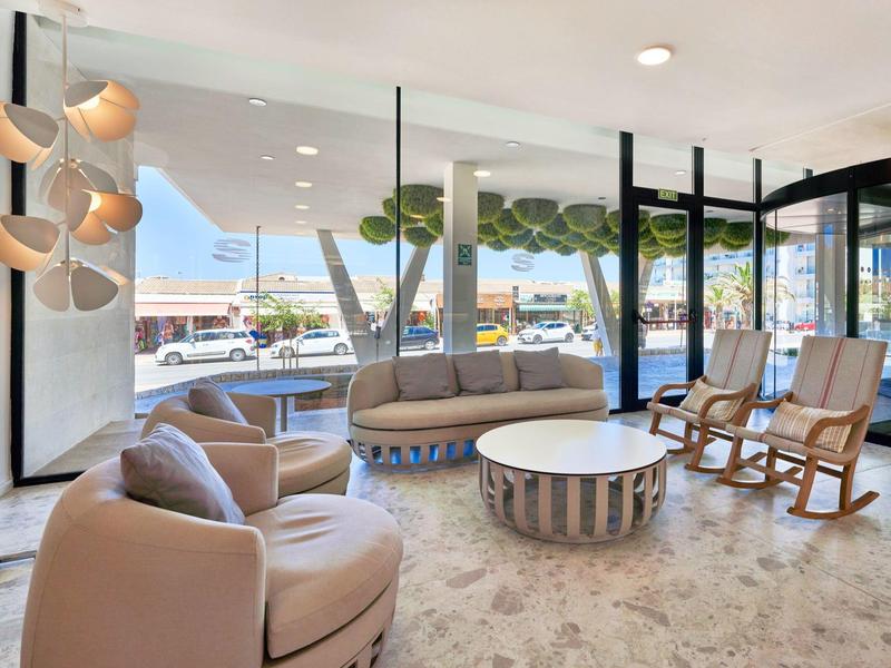 Bright hotel lobby with cozy armchairs, a round table, and large windows overlooking outside.