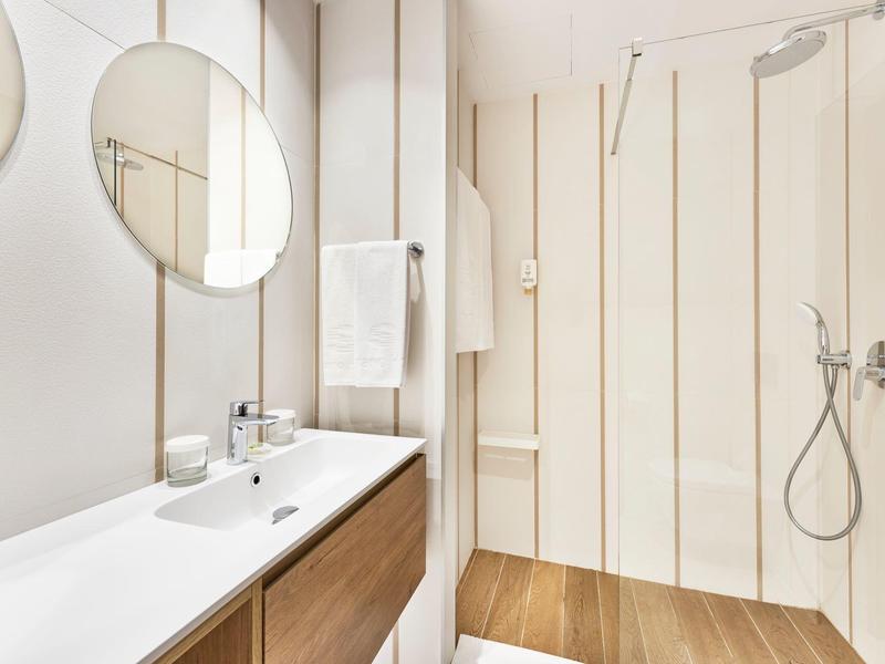 Modern bathroom with double sink, two round mirrors, and walk-in shower with wooden floor.