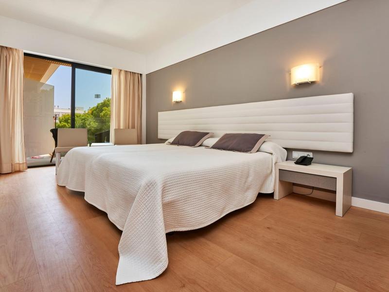 Bright hotel room with double bed, nightstands, and large window overlooking outdoor area.