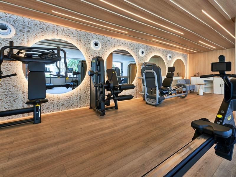 Modern gym with exercise equipment, large mirror, and wooden floor in a hotel.