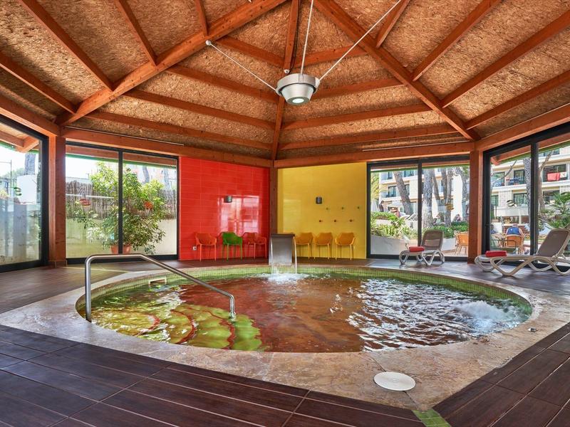Interior of a hotel with a round hot tub, large windows, and wooden flooring.