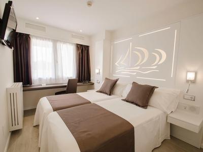 Helles Hotelzimmer mit zwei Betten, braunen Kissen, Vorhängen und moderner Wanddeko aus Licht.