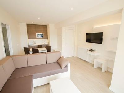 Helles Wohnzimmer mit großer Eckcouch, Wand-TV und offenem Kücheneck mit Mikrowelle.