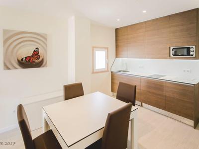 Moderne Küche mit braunen Schränken, weißer Arbeitsplatte, kleinem Fenster und Essbereich mit vier Stühlen.