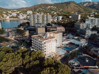 Stadtansicht mit mehreren Wohngebäuden, Bergen im Hintergrund und bewaldeten Flächen im Vordergrund.
