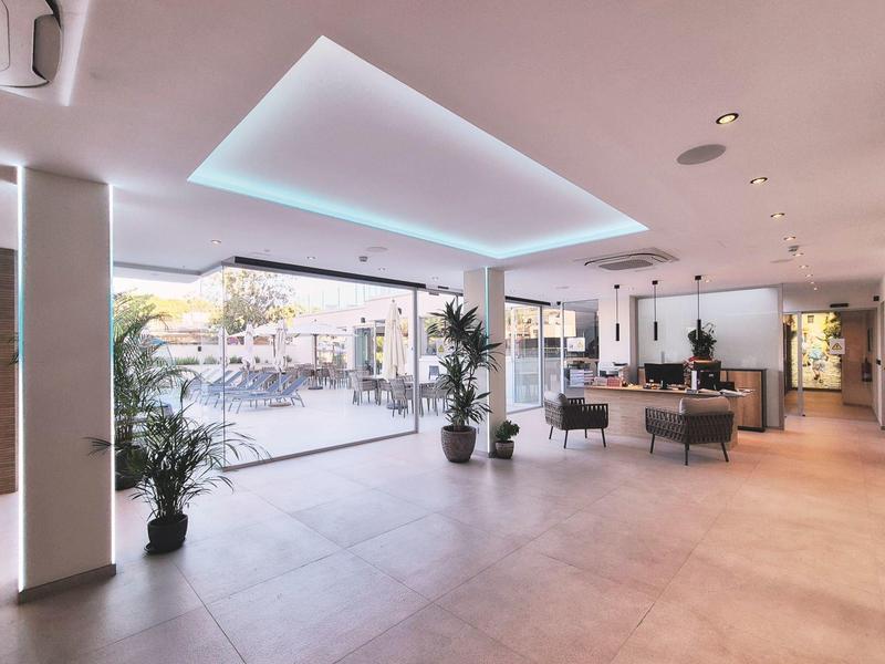 Hall d'hôtel lumineux avec éclairage moderne, plantes et accès à un espace extérieur.